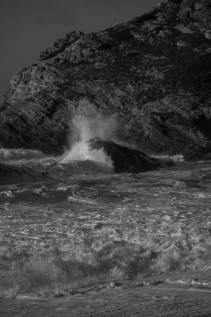 Black and white image of waves crashing on a rocky ocean shoreline, capturing nature's raw power.